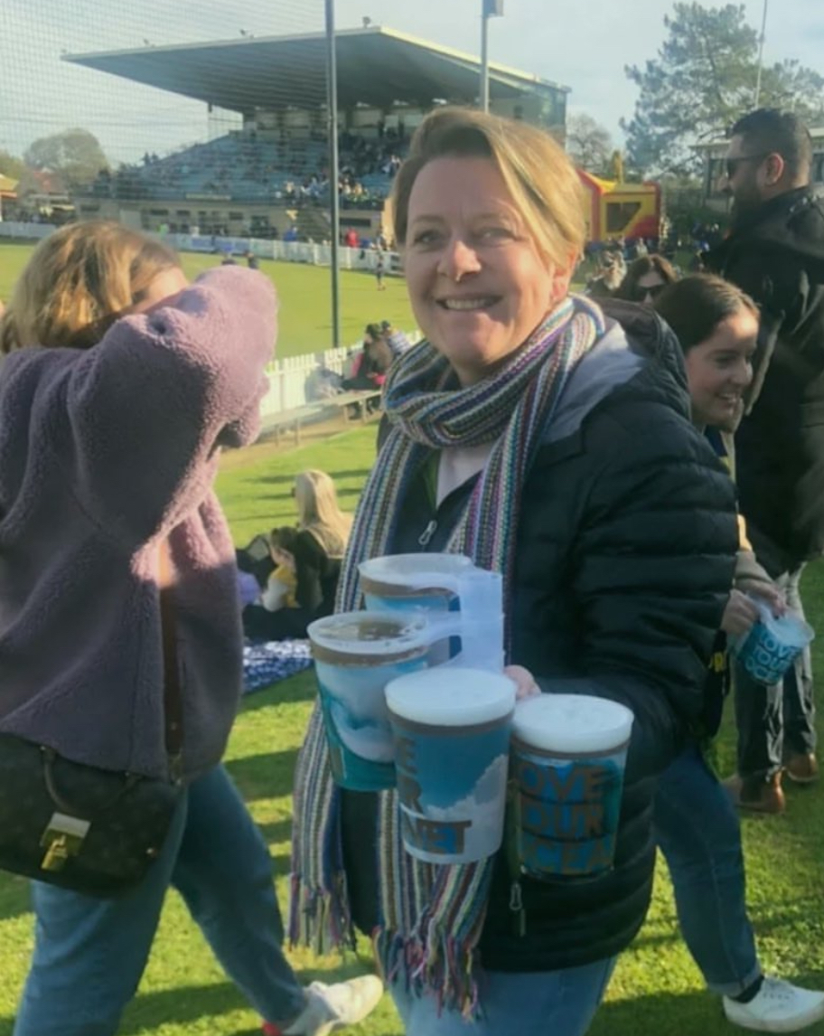 A festival-goer carrying several branded reusable cups at an outdoor sports ground